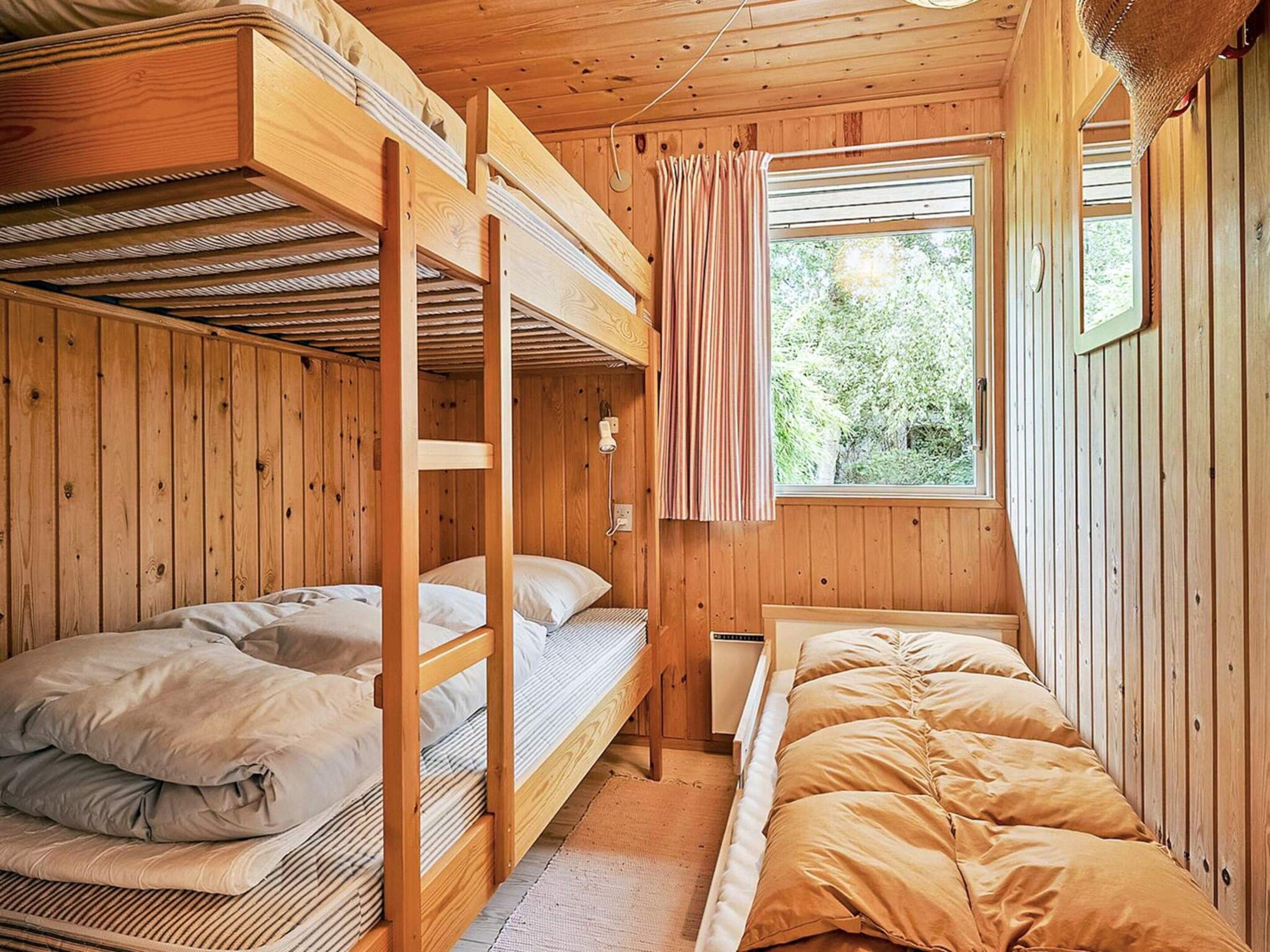 A cabin with bunk beds, a window with curtains, and a wooden interior.