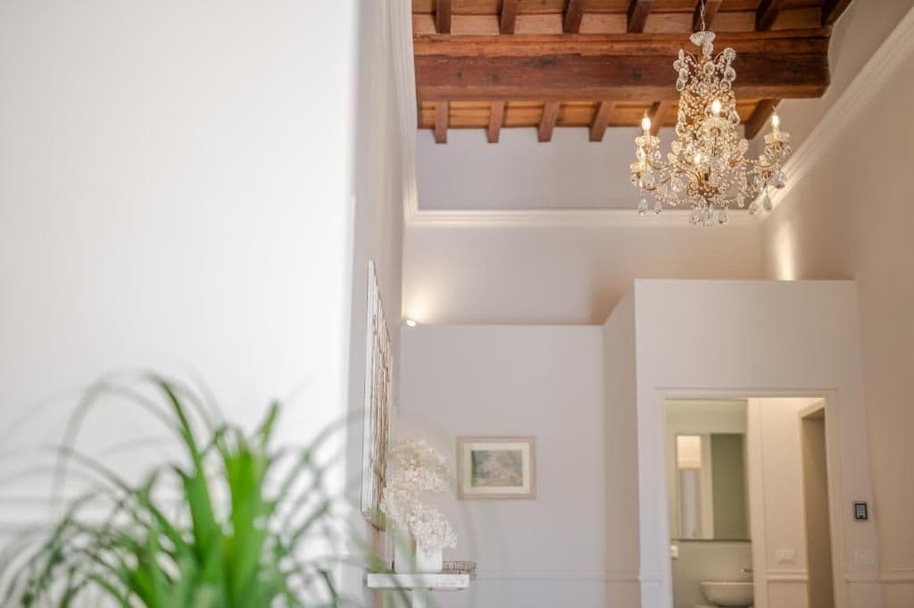 Ein Zimmer mit einer Kandelaber, Holzbalkendecke, einer weißen Wand und einem Durchgang zu einem anderen Raum.