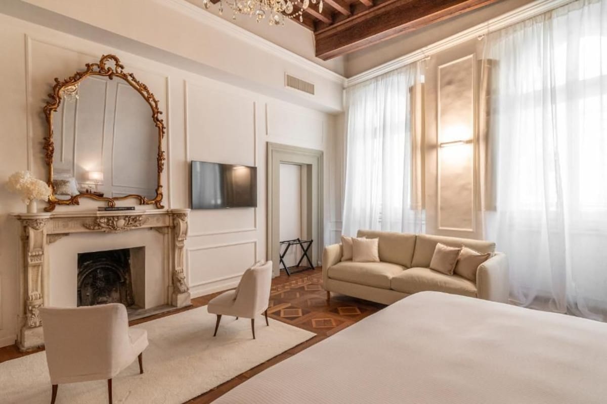 Een hotelkamer met een open haard, een grote spiegel, een bank en een bed.
