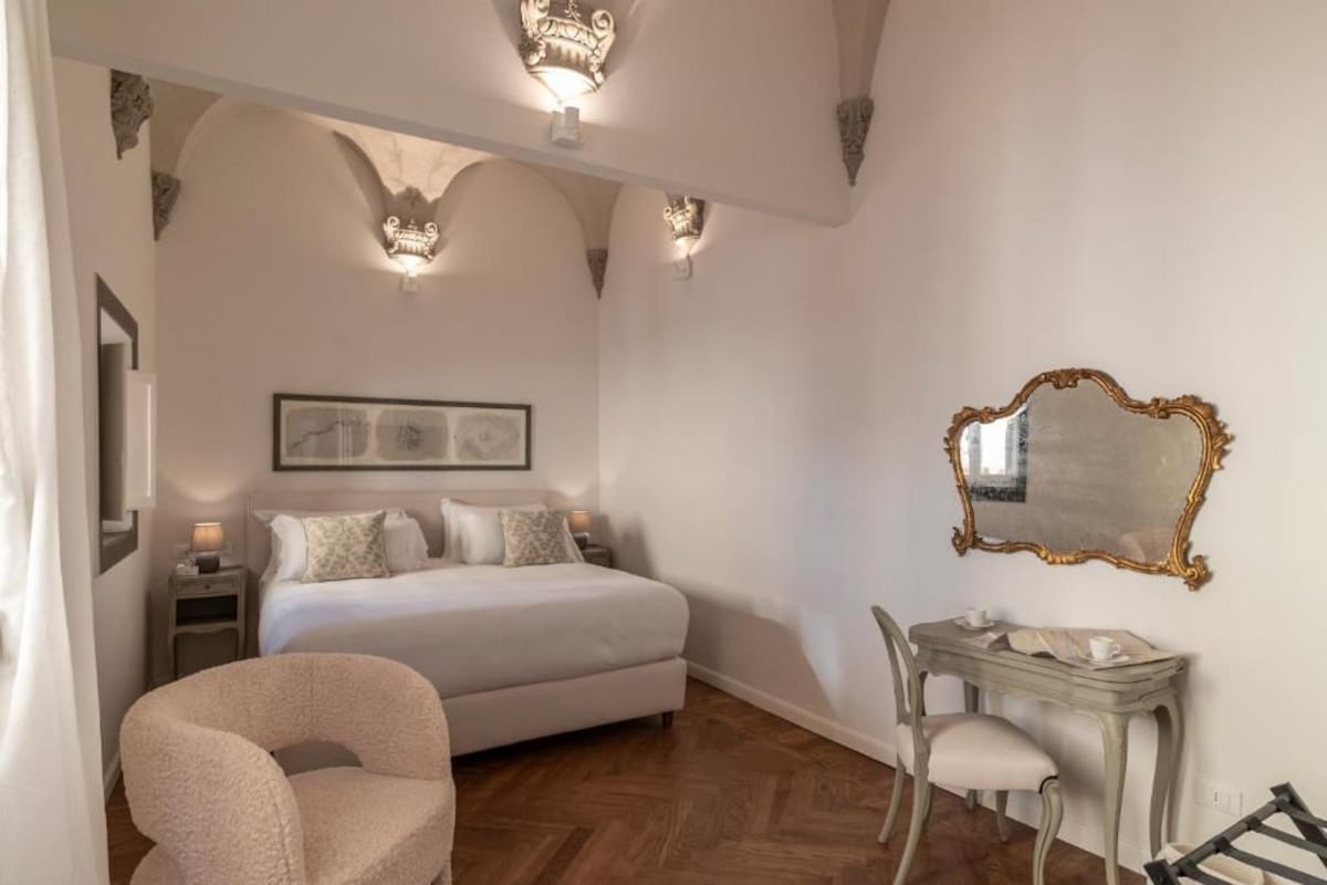 Een slaapkamer met een bed, een stoel, een tafel en een spiegel.