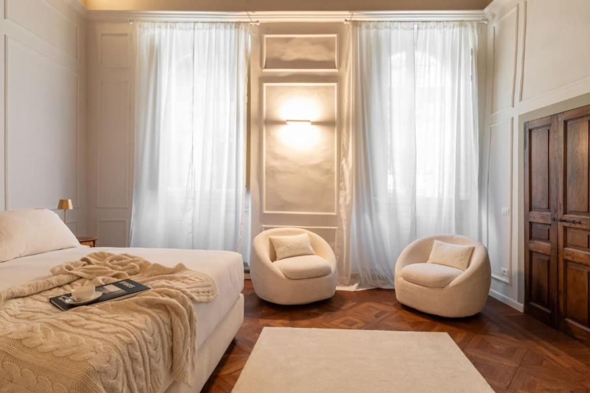 Een hotelkamer met een bed, twee fauteuils, een vloerkleed en een wandlamp.