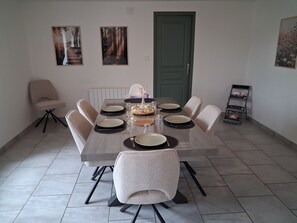 Een eethoek met een rechthoekige tafel gedekt voor zes personen, omringd door zes stoelen, met kunstwerken aan de wanden en een deur op de achtergrond.