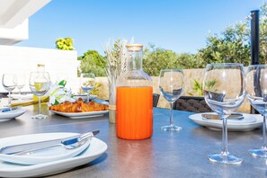 Ein Tisch für ein Essens im Freien, gedeckt mit Tellern, Gläsern und einer Flasche orangefarbene Flüssigkeit.