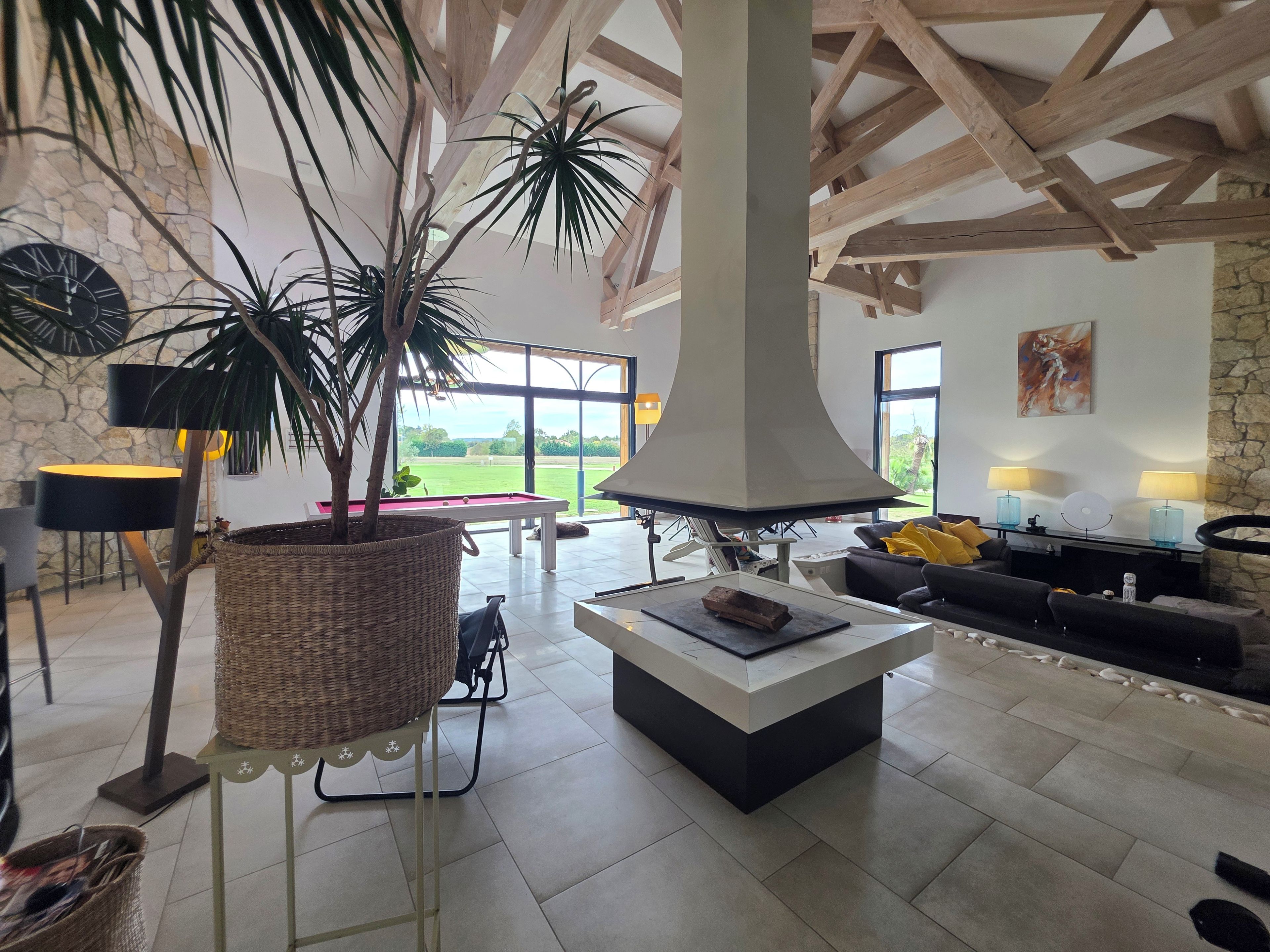 A spacious living area with a pool table, a fireplace, and a view of a green field through large windows.