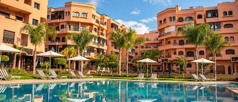 A hotel with a swimming pool, multiple balconies, and palm trees.