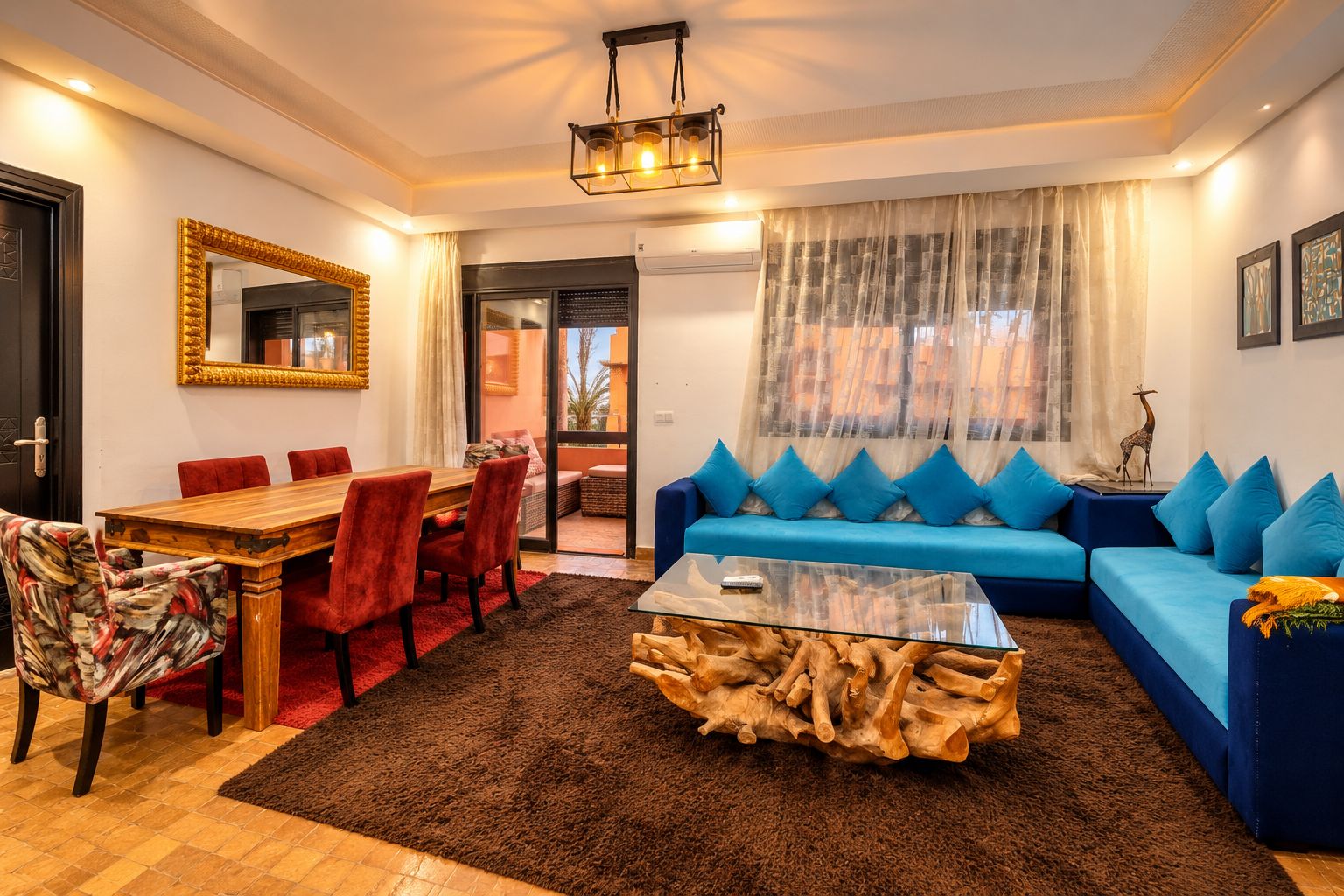 A living room with a blue sofa, red chairs, a wooden dining table, and a glass coffee table.
