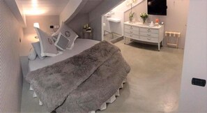 Une chambre à coucher avec un lit, un tapis moelleux, une commode et un téléviseur fixé au mur.
