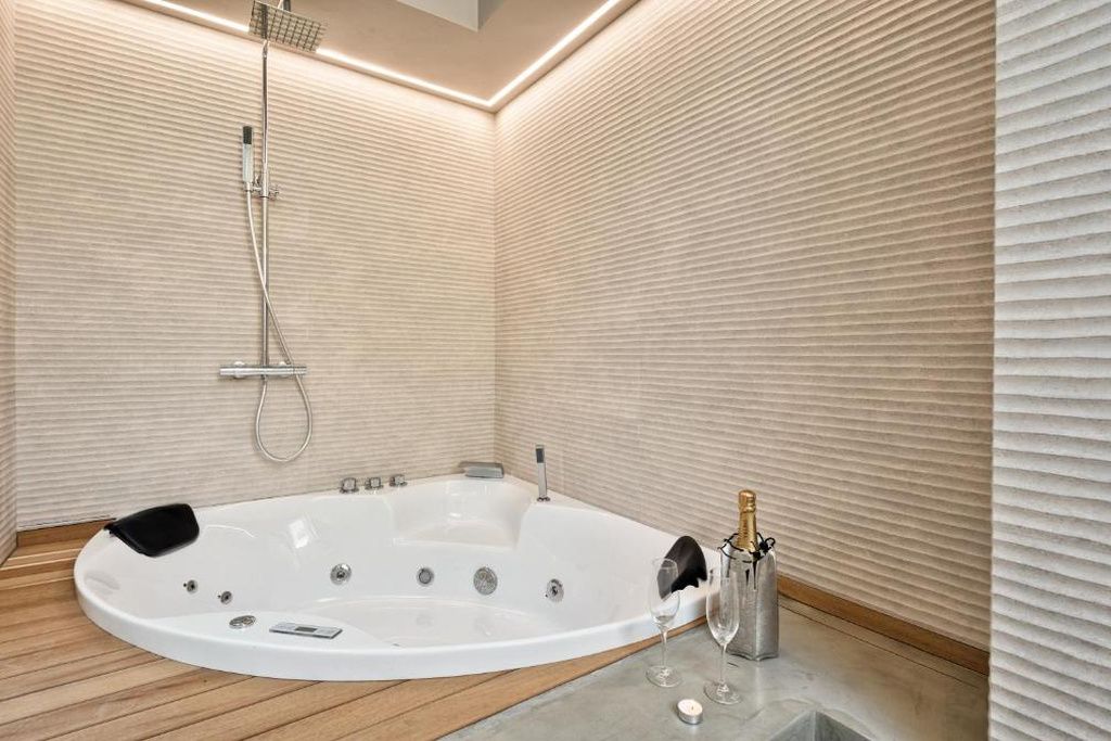 A modern bathroom with a freestanding bathtub, a handheld showerhead, and a champagne bottle.