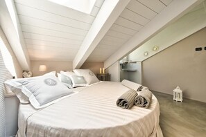 Een slaapkamer met dakraam, een bed met kussens en een opgerolde handdoek, een nachtkastje met lamp en een kleine lantaarn.