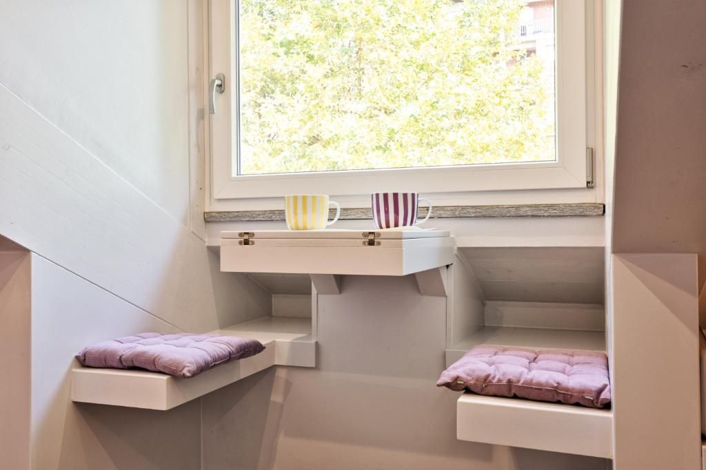 A room with a window, a shelf with cups, and two cushioned seating areas.