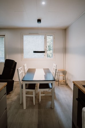 A dining area with a table and chairs, a window with blinds, and a ceiling light fixture. - Tyylikäs kaksio keskustan tuntumassa (Lappeenranta)