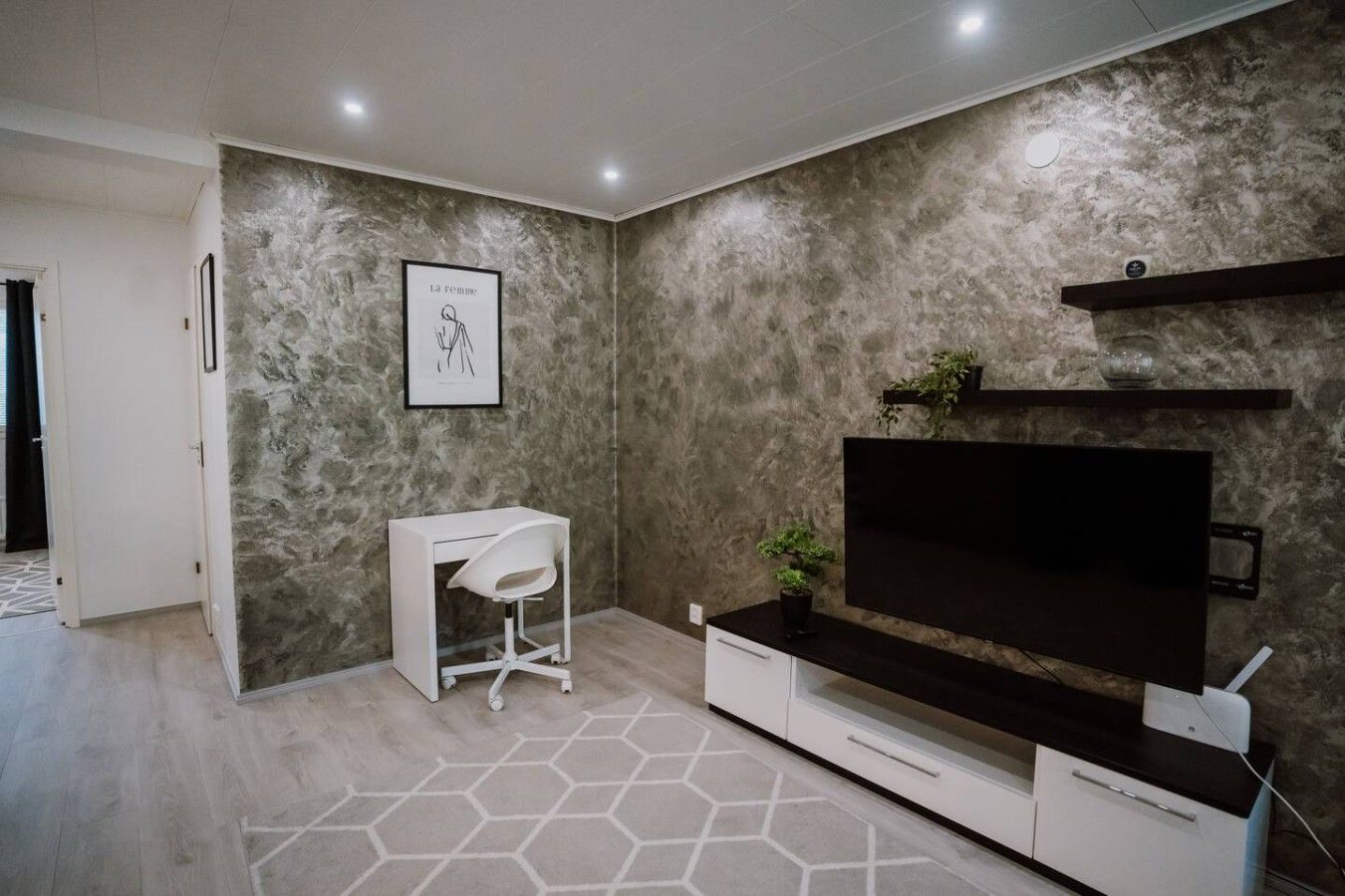 Un salon moderne doté d’un grand téléviseur à écran plat, d’un bureau blanc et d’un sol à motifs hexagonaux.