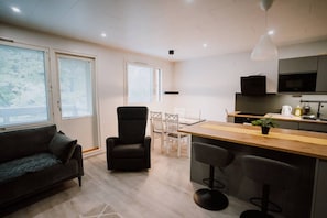 A modern living space with a sofa, a dining table, chairs, a kitchen area with a microwave, and a bar stool. - Tyylikäs kaksio keskustan tuntumassa (Lappeenranta)