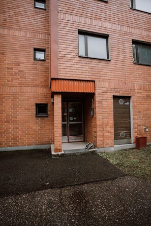 Un bâtiment en briques doté d’une grande fenêtre, d’une porte avec une poignée en métal et d’une petite fenêtre située au-dessus de la porte.