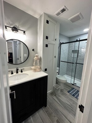 A modern bathroom with a double sink, a large mirror, a shower enclosure, and a small step leading to the toilet. - Putt & pool in Raleigh (Raleigh)