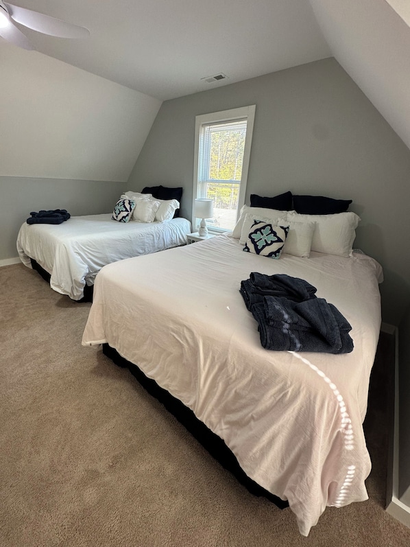 A bedroom with two beds, a window, and a ceiling fan.