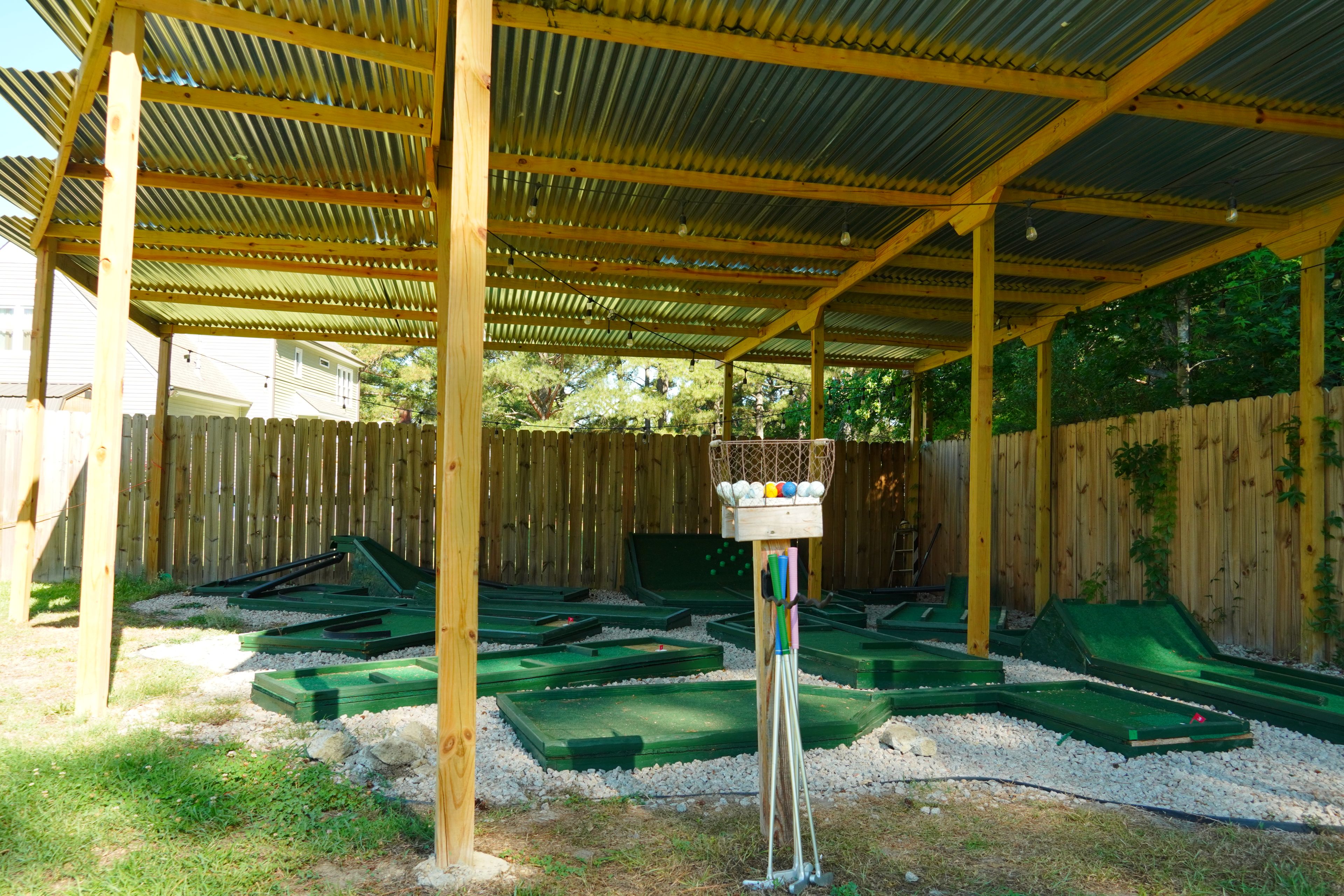 A covered outdoor area with a wooden structure, green tables, and a bird feeder.