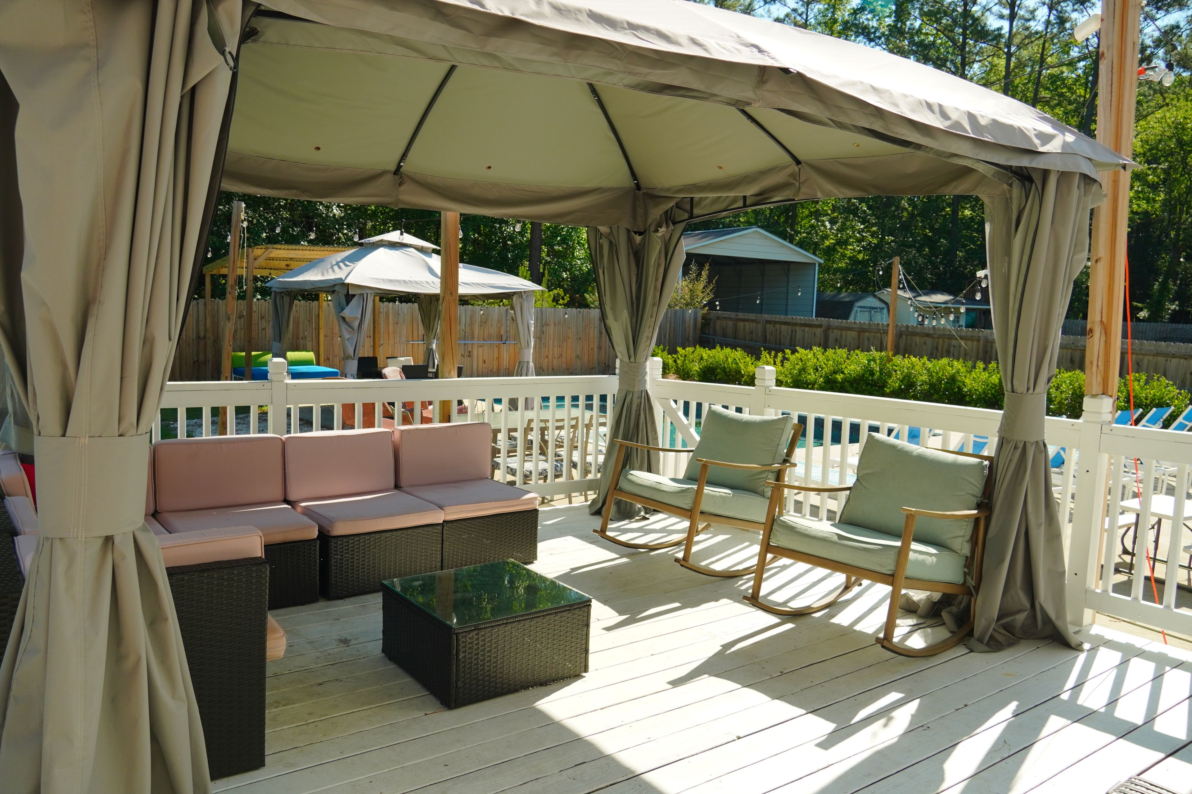 A covered outdoor seating area with cushioned benches and chairs, a glass-top table, and a wooden deck.