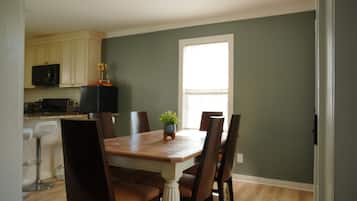 A dining area with a wooden table, six chairs, a potted plant, and a window.