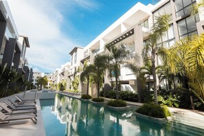 Un hotel moderno con piscina, tumbonas y exuberante vegetación.