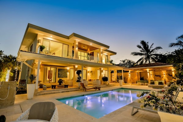 Uma casa moderna de dois andares com piscina, área de estar externa e um pátio bem iluminado.