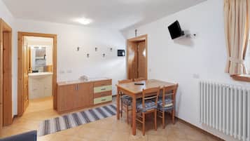 Ein Zimmer mit Esstisch, Stühlen, einem Schrank, einem an der Wand montierten Fernseher und einer Heizung.