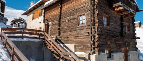 A wooden log cabin with a wooden staircase leading up to the entrance, surrounded by snow.