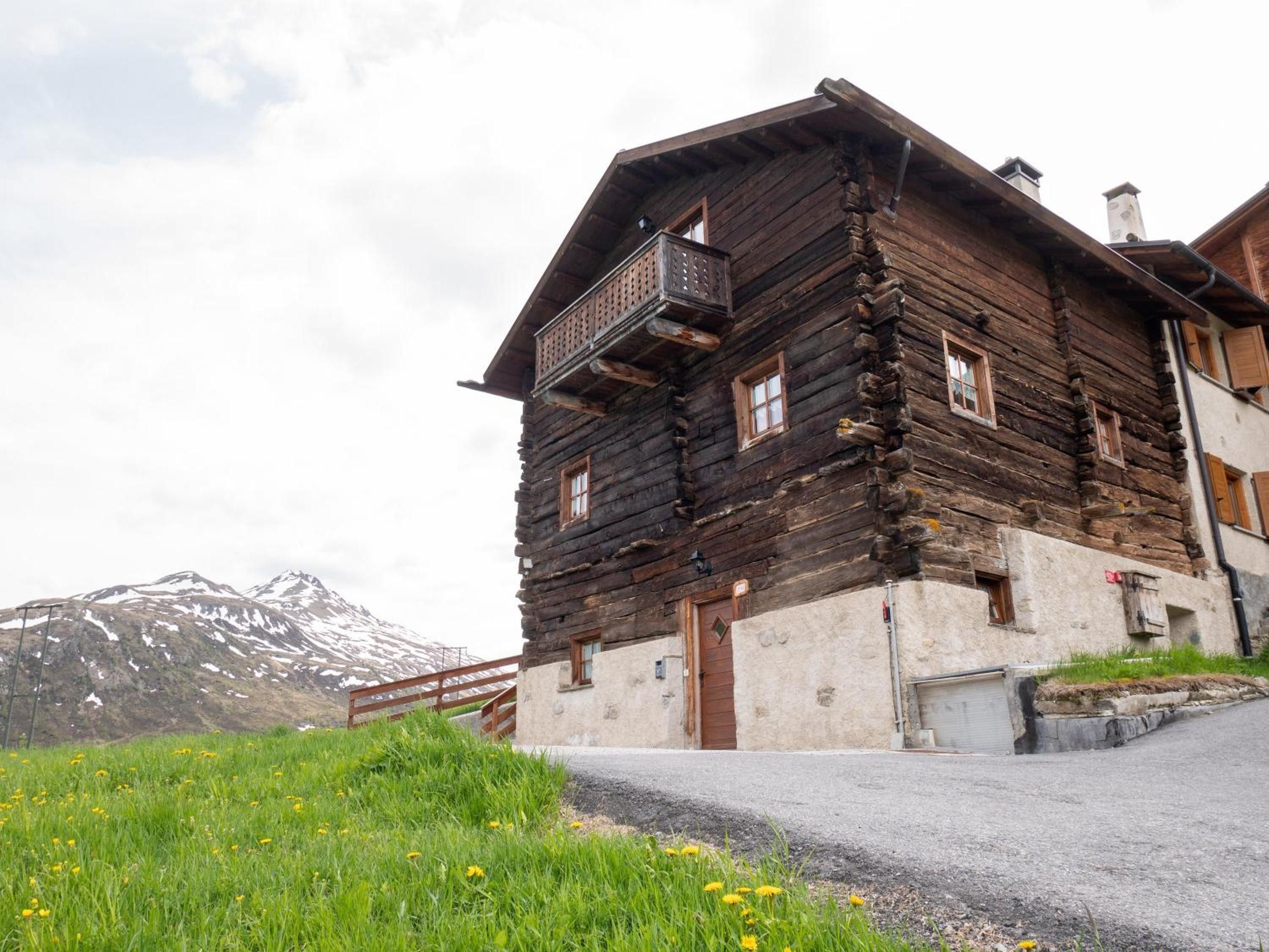 Un chalet rustique en rondins de bois, doté d’un balcon, qui se dresse sur un fond de montagnes.