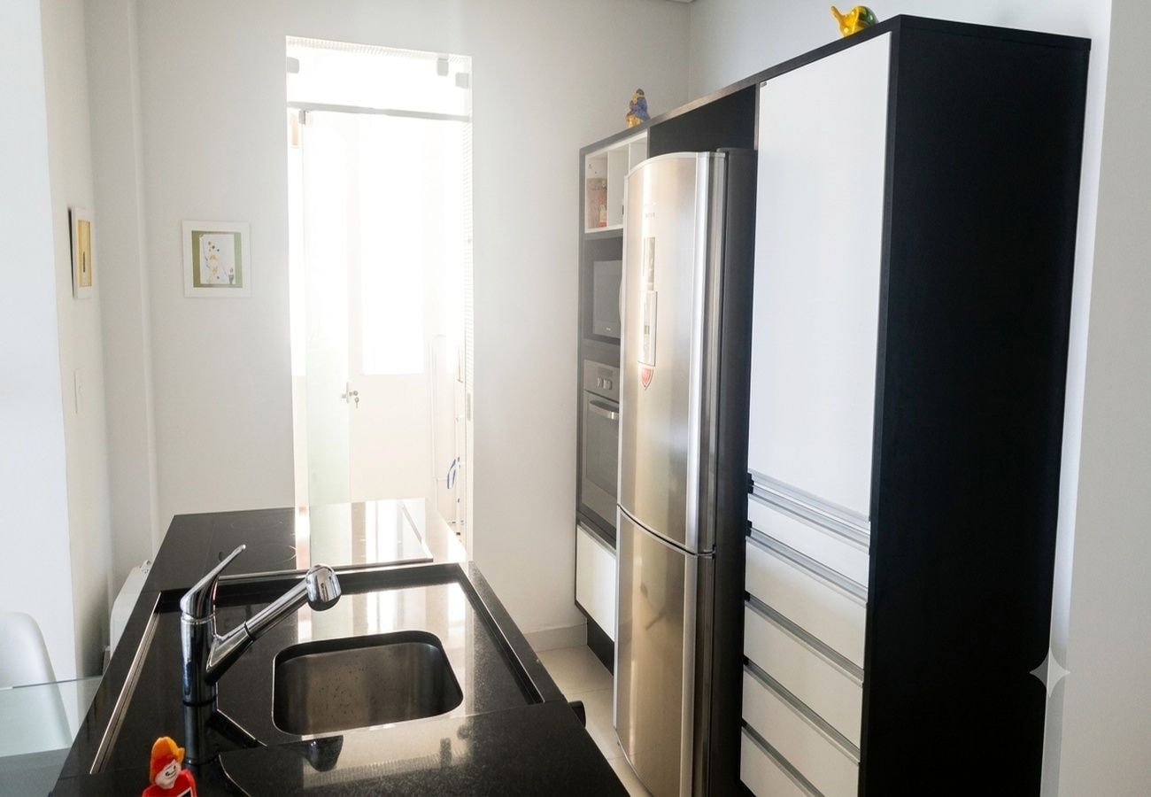 Une cuisine de taille réduite, dotée d’un réfrigérateur en acier inoxydable, d’un évier et d’un plan de travail noir.