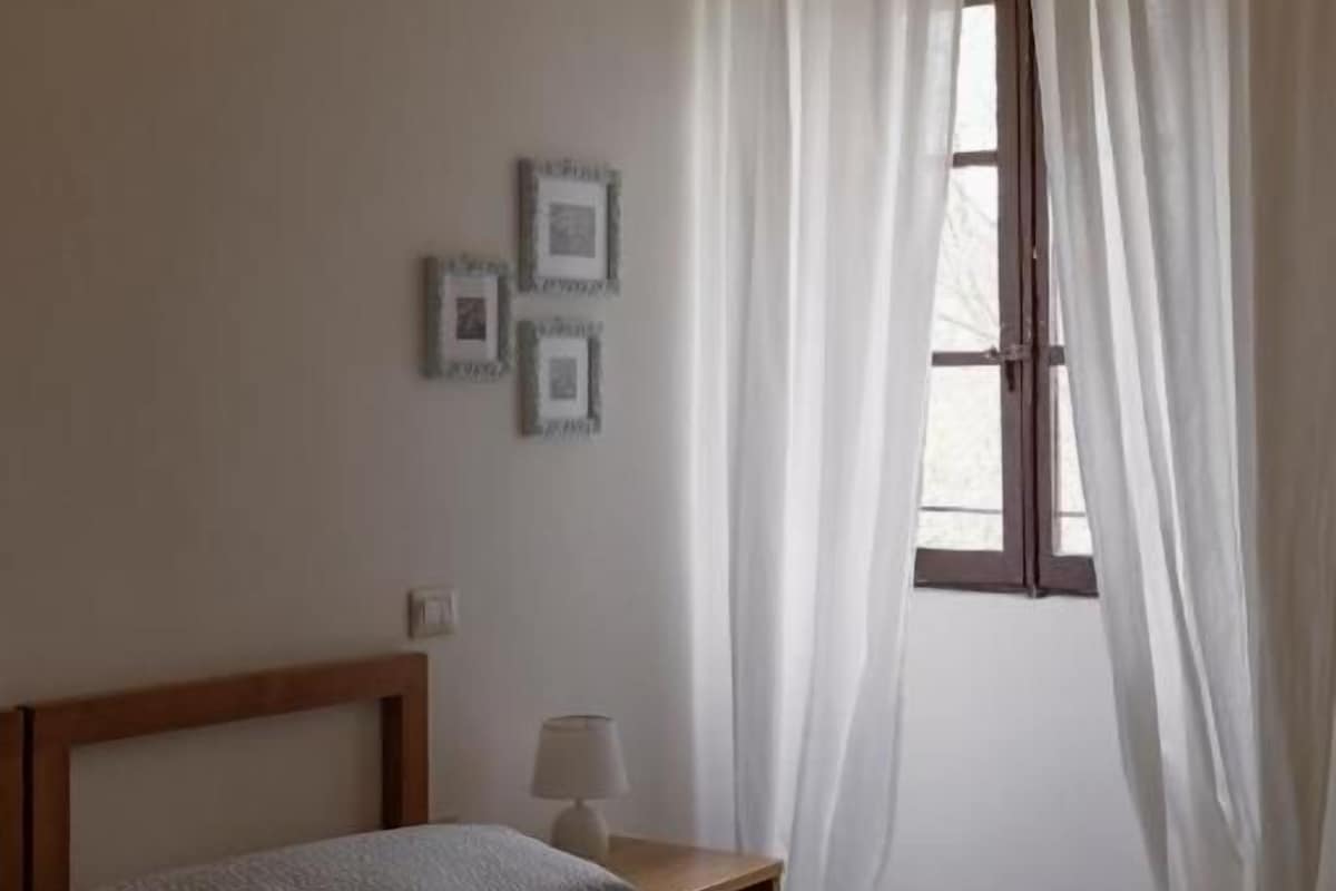 Une chambre à coucher avec un lit, une table de chevet, une lampe et une fenêtre avec des rideaux.