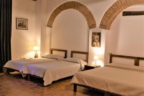 Une chambre d’hôtel avec deux lits, une arche en briques, une table de chevet avec une lampe et un tableau encadré au mur.