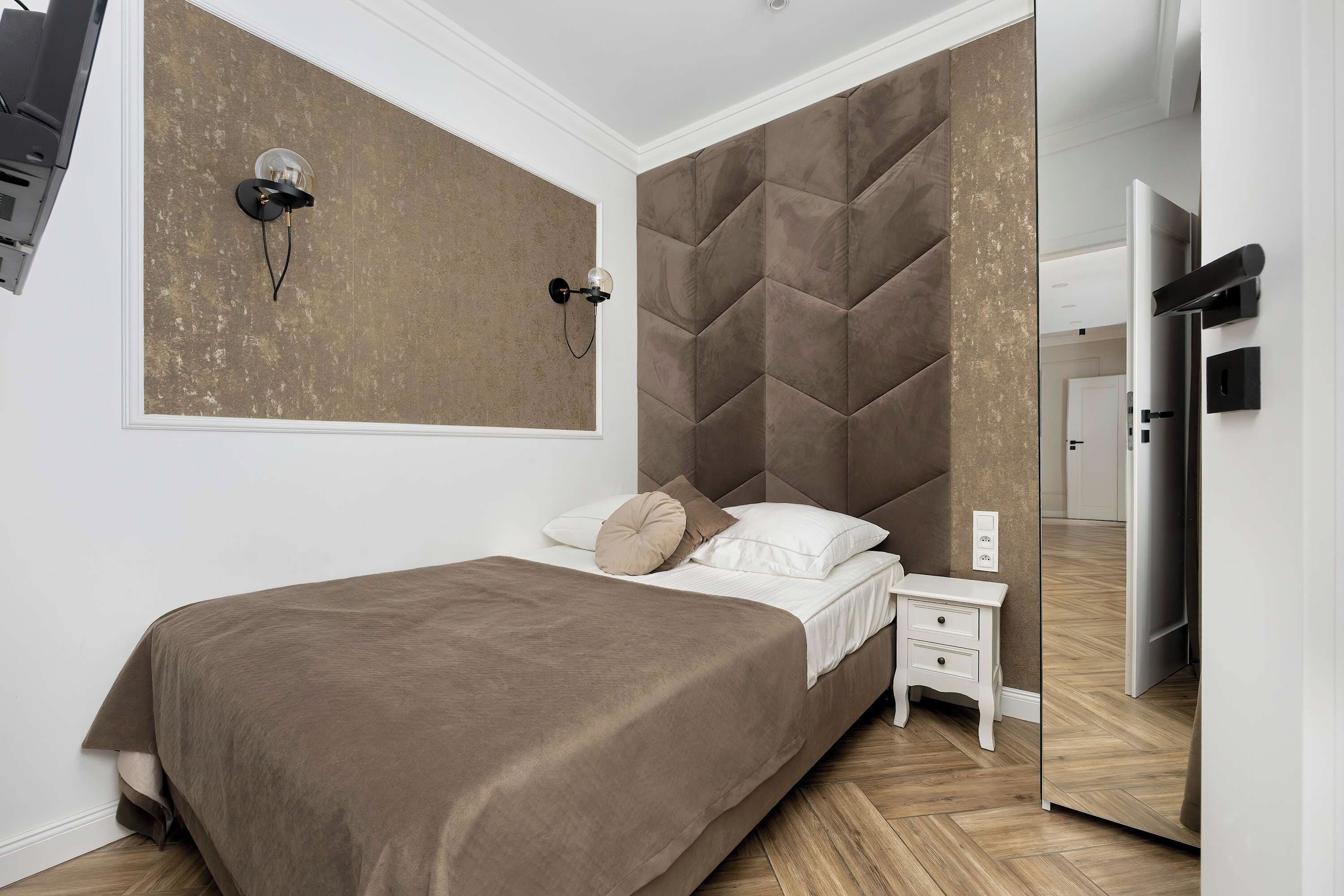 A bedroom with a bed, bedside table, wall-mounted lamp, and a mirror.