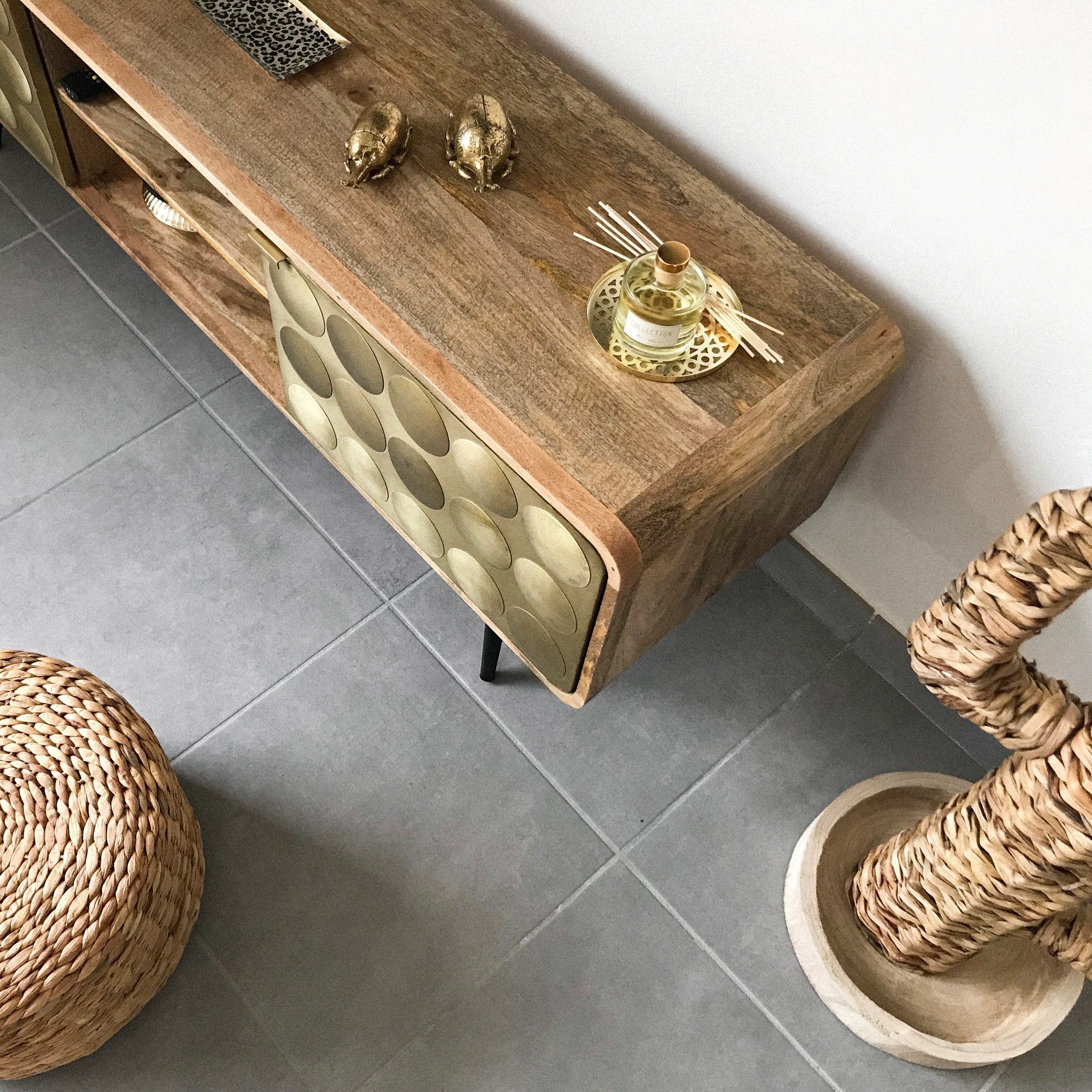 A wooden console table with a decorative pattern, a bottle of cologne, and two golden beetles.