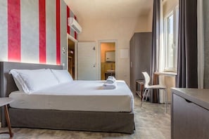 Hotellihuone, jossa on sänky, työpöytä, tuoli, vaatekaappi, ikkuna ja ovi.