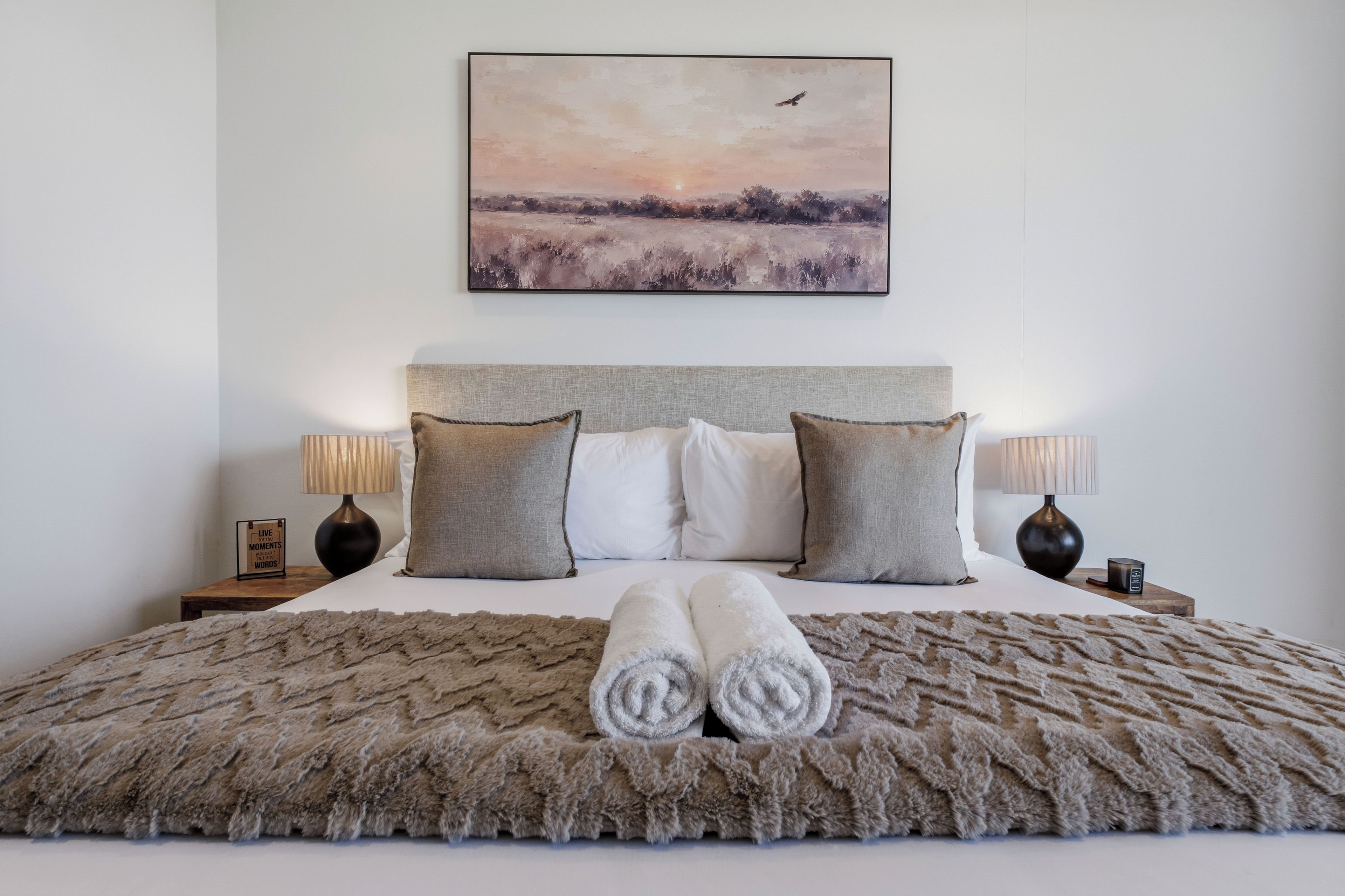 Ein ordentlich bezogenes Bett mit einer flauschigen Decke, zwei Kissen und einem Paar zusammengerollter Handtücher.