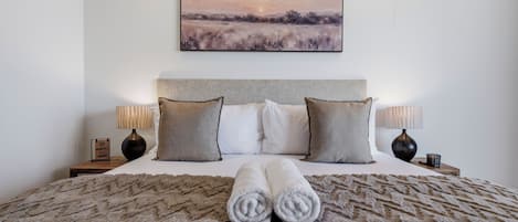 Una cama bien hecha con un edredón mullido, dos almohadas y un par de toallas enrolladas.