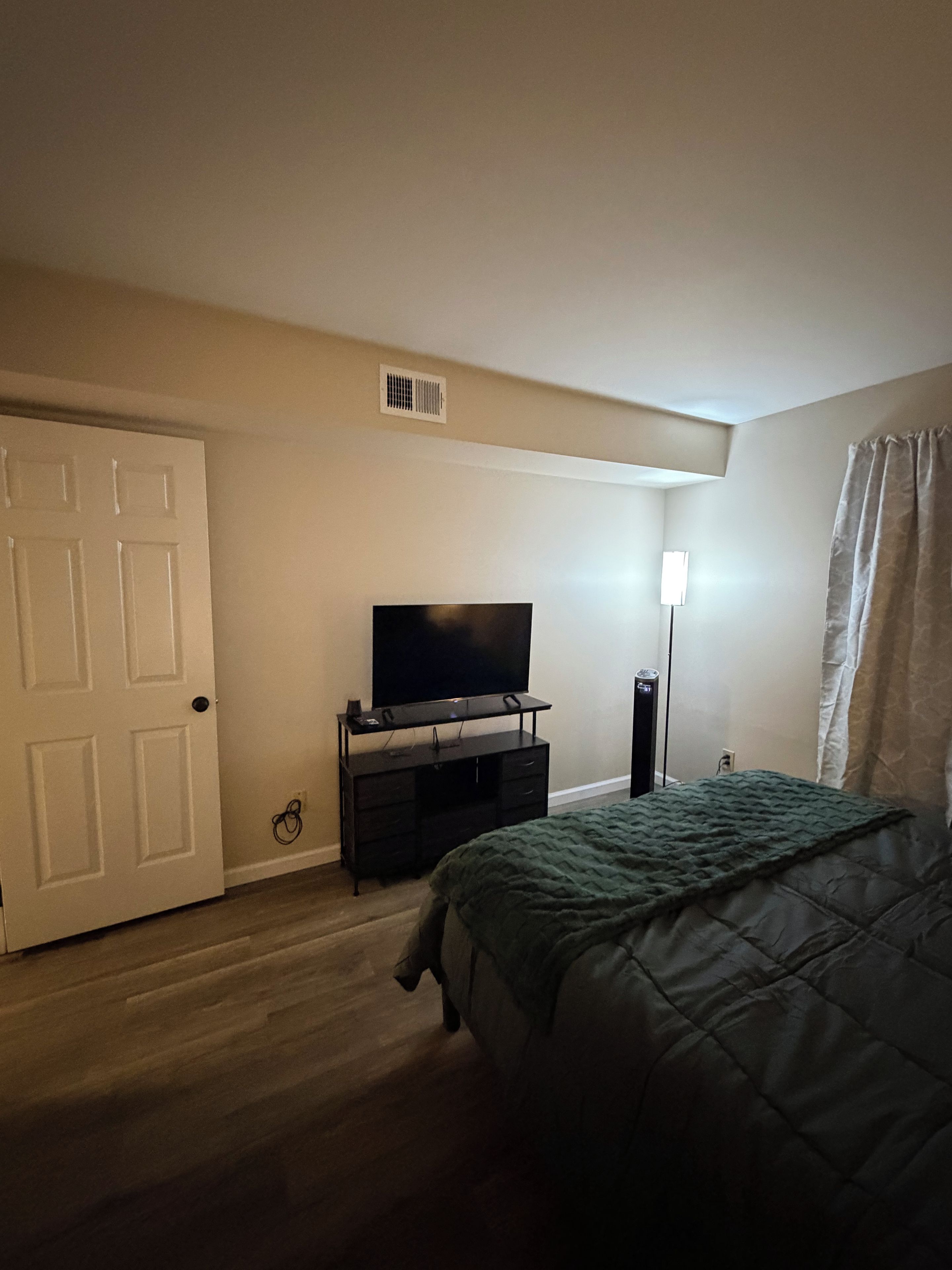 Une chambre à coucher avec un lit, un téléviseur posé sur un meuble, une porte et un luminaire.