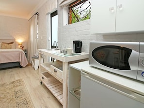 Une chambre compacte comprenant un lit, une petite table de chevet, un four à micro-ondes encastré et une fenêtre donnant sur un espace verdoyant.