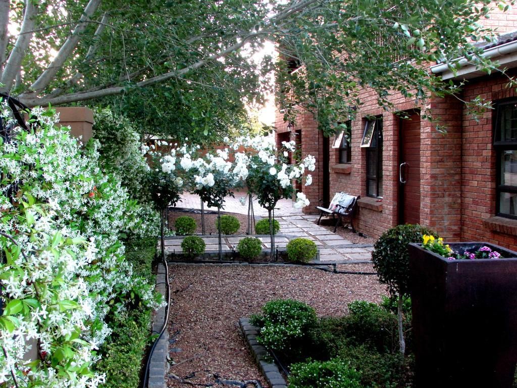 A courtyard with a brick building, a paved patio, and a garden area with shrubs and flowering plants.