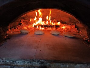Kiviuuni, jonka sisällä palaa puuta, ja uunin pohjalla neljä leipää.