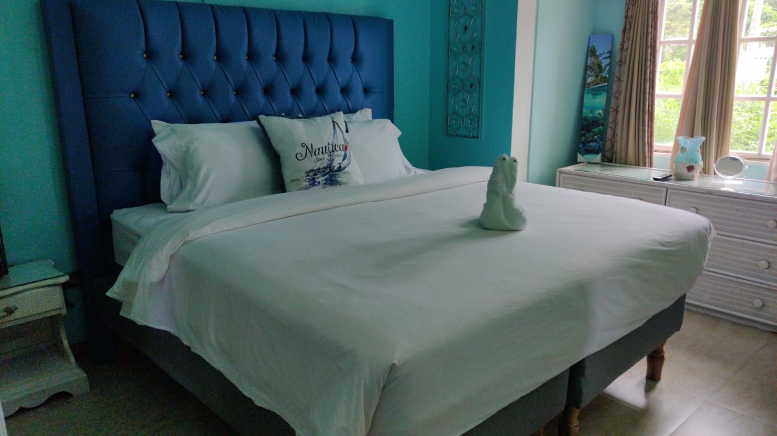 Una cama con cabecera capitonada, ropa de cama blanca y un cojín decorativo con texto.
