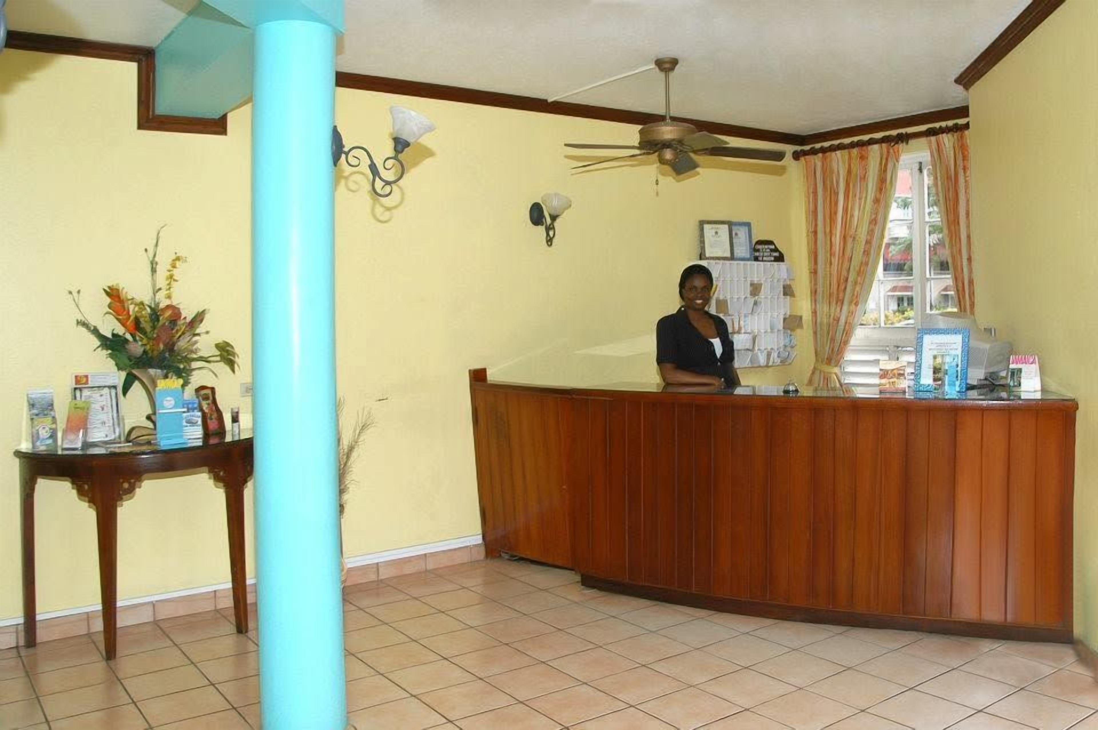Uma área de recepção com balcão de madeira, ventilador de teto, luminária na parede e uma janela com cortinas.