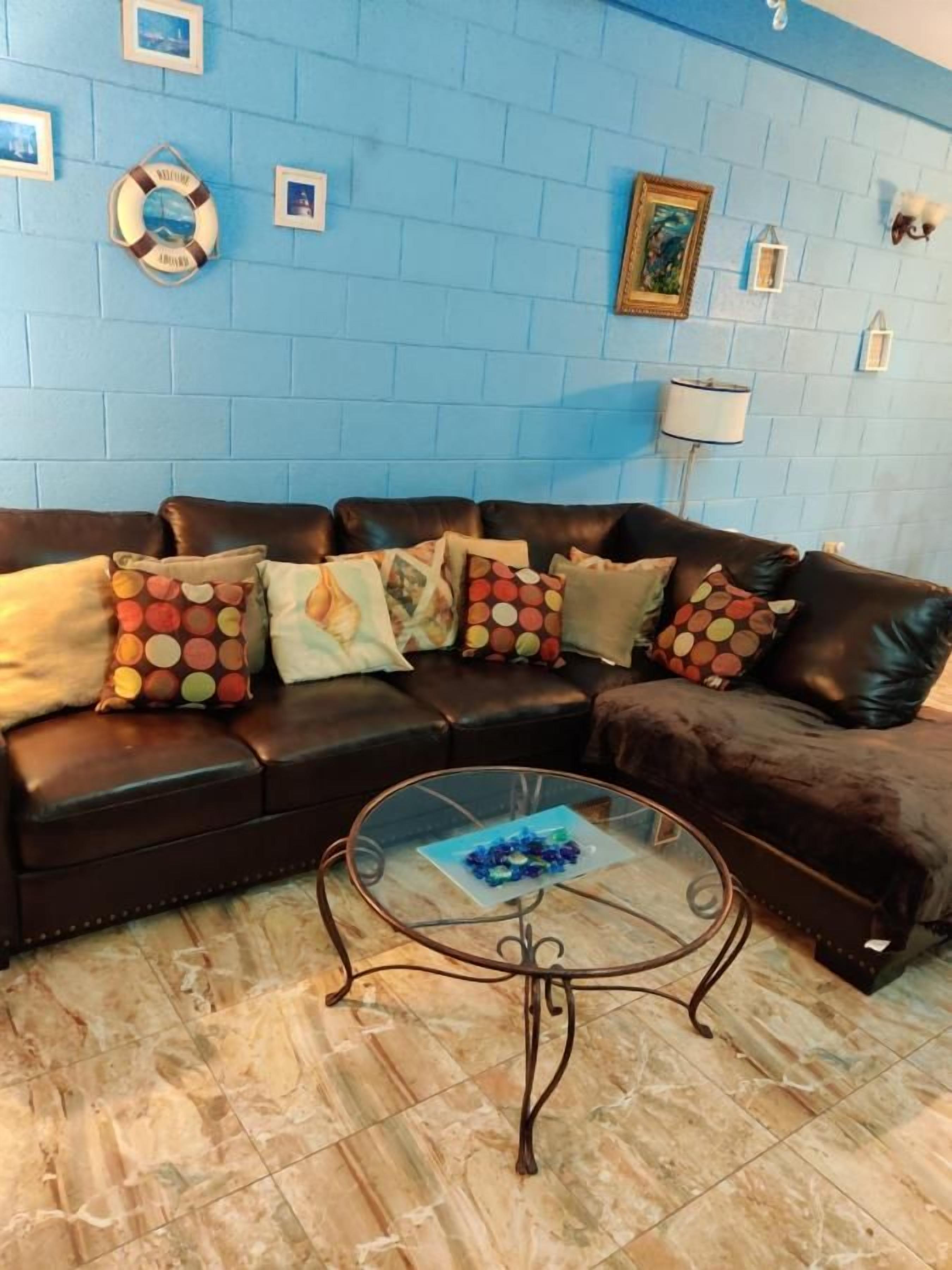 Una sala de estar con una pared de ladrillo azul, un sofá de cuero marrón y una mesa de centro de vidrio.