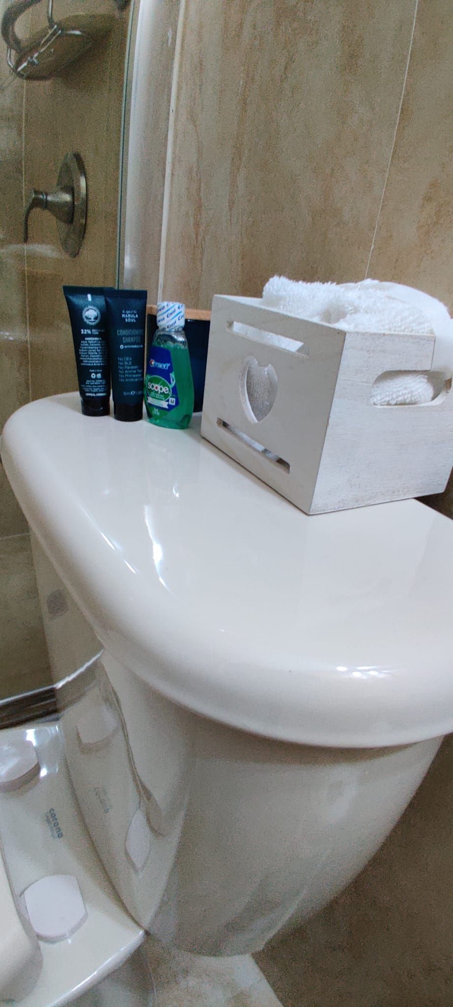 A bathroom with a toilet, a shower, and toiletries on the toilet.