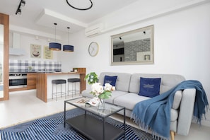 A modern living room with a sofa, coffee table, and a kitchen area in the background. - Warsaw | Międzynarodowa 31A | Spacious Apartment | Air conditioning (Warszawa)