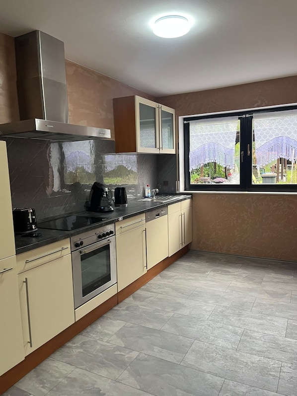 A kitchen with a built-in oven, a coffee maker, and a window with a view of greenery.