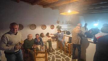 Un gruppo di persone in una stanza con pavimento in pietra, soffitto in legno e un angolo bar con bottiglie e bicchieri.