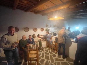 Un grup de persones en una habitació amb sòl de pedra, sostre de fusta i zona de bar amb ampolles i vasos.