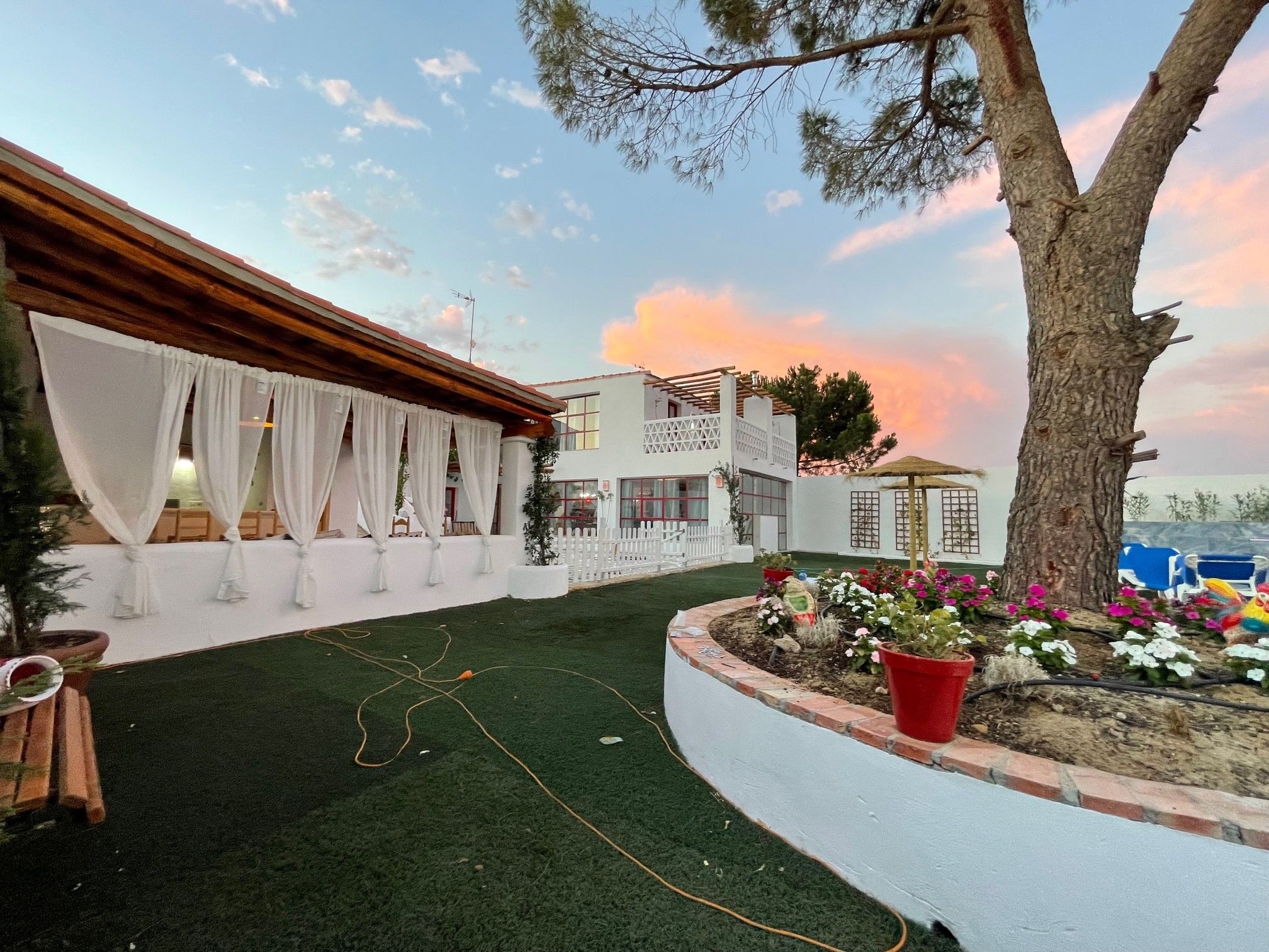 A courtyard with a green artificial turf, white curtains, and a white fence.