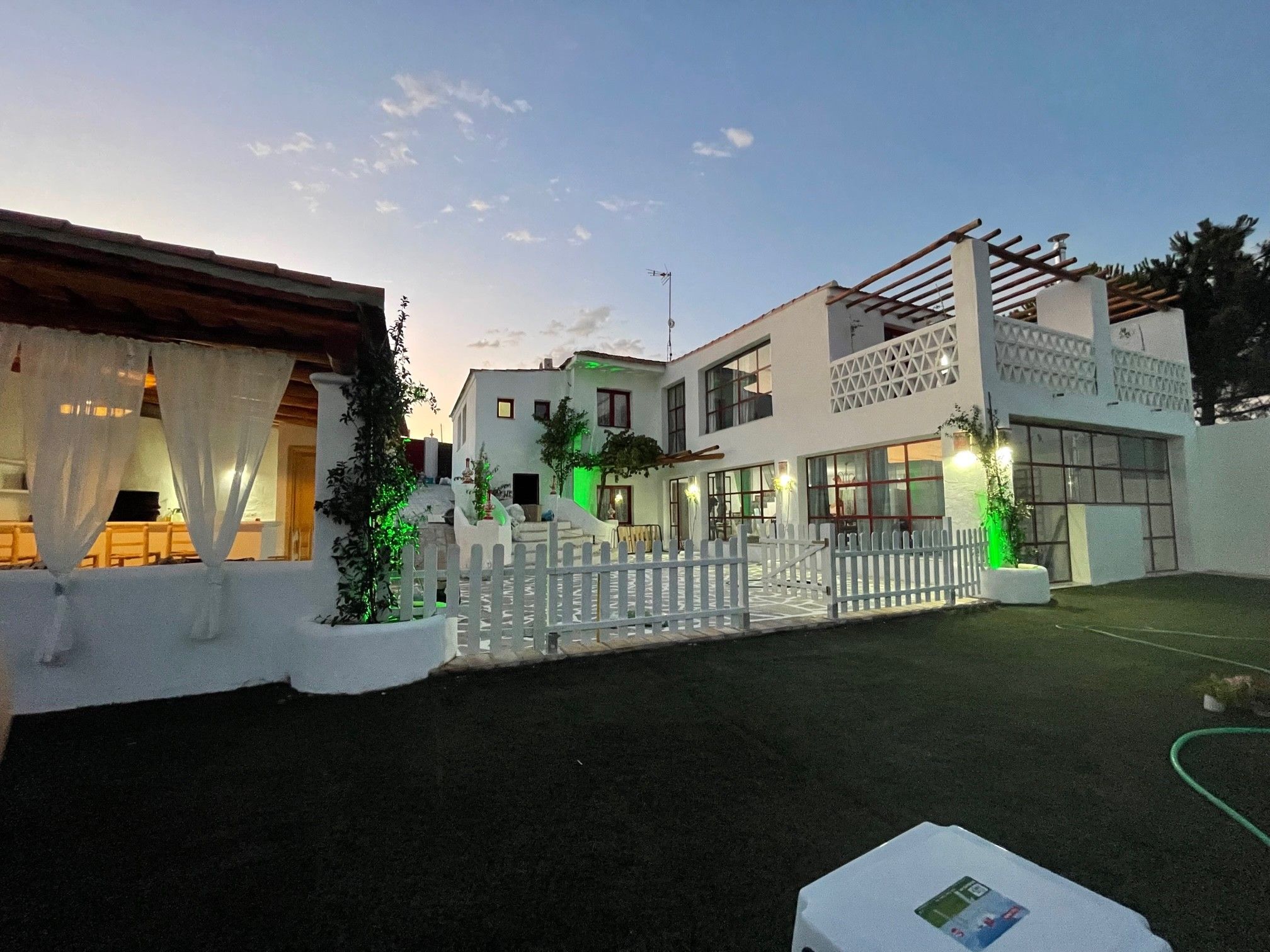 Un edificio moderno de dos plantas con fachada blanca, un patio cercado y un área de estar al aire libre cubierta.